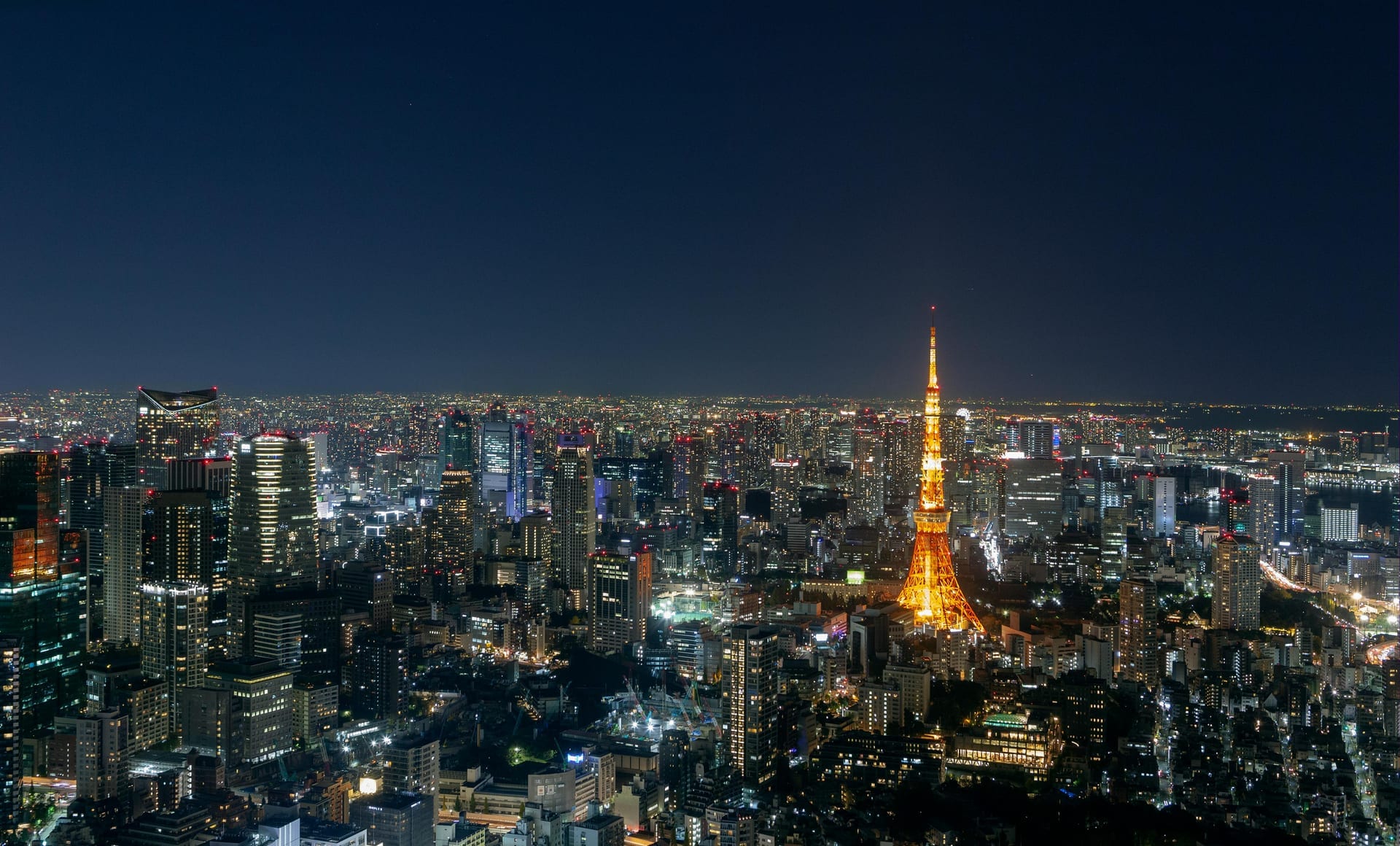 Tokyo Tower glowing orange at night surrounded by the illuminated city skyline from above